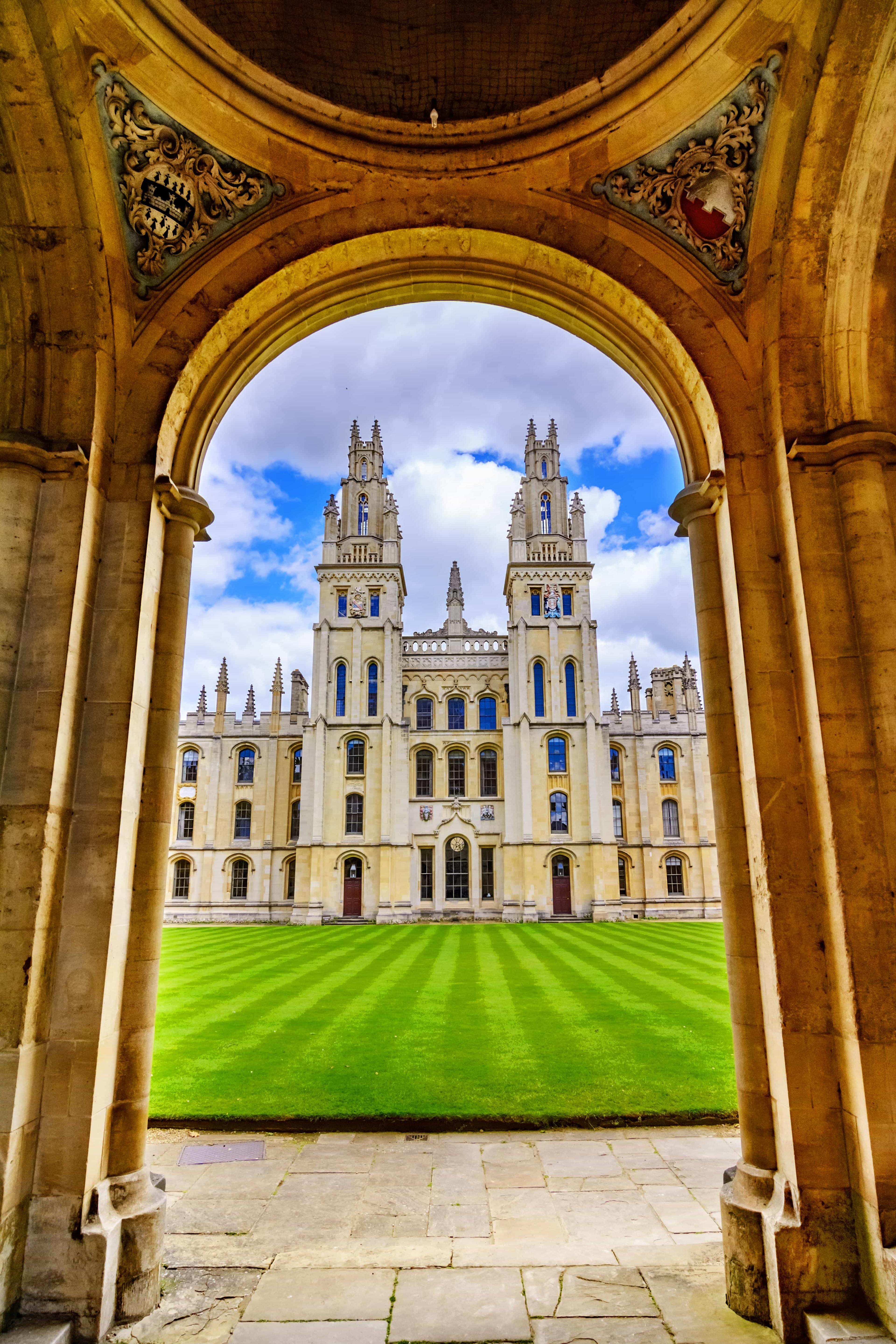 An archway frames an old UK university building, offering a quaint view through its historic entrance.