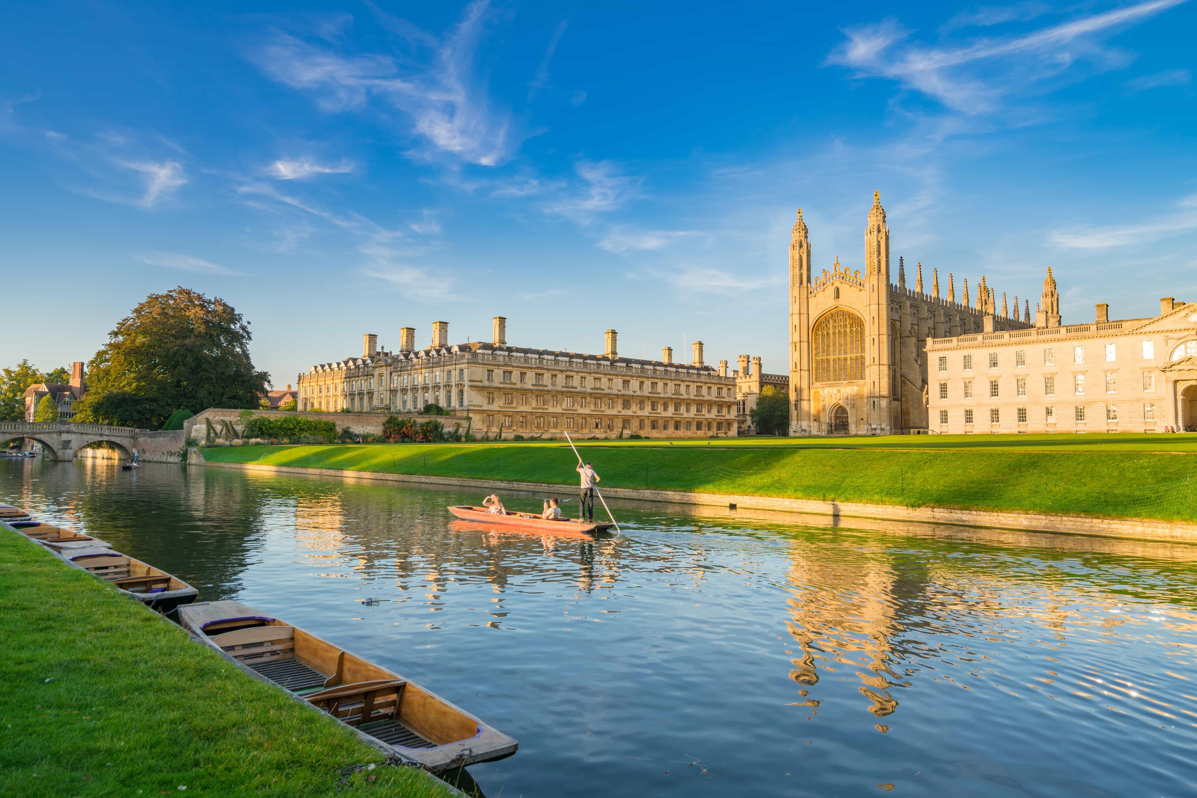 Cambridge university building stands beside the River Cam, where a river boat is taking visitors on a tour.