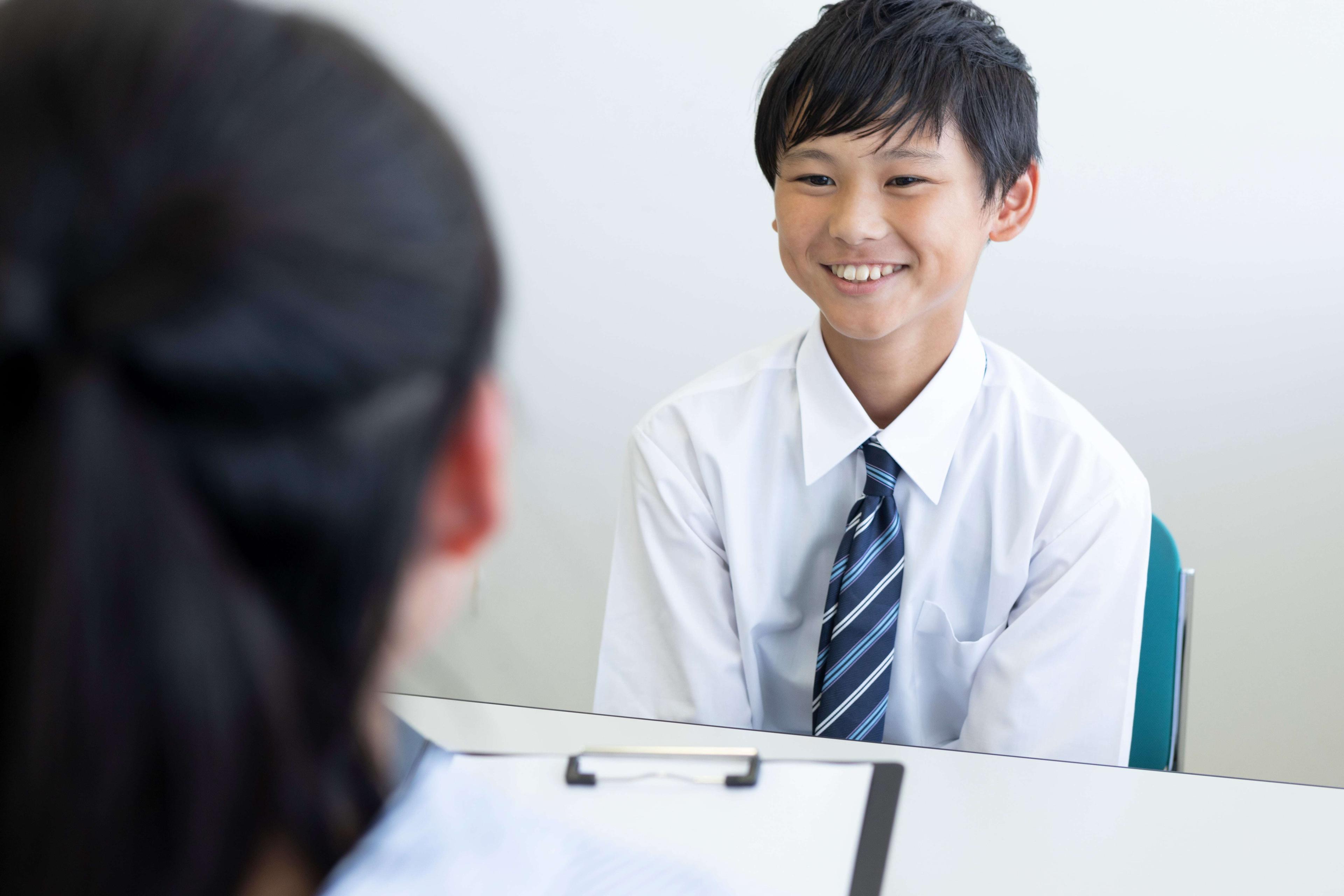 A young student smiles warmly at the school interviewer as he prepares for a school admissions interview.