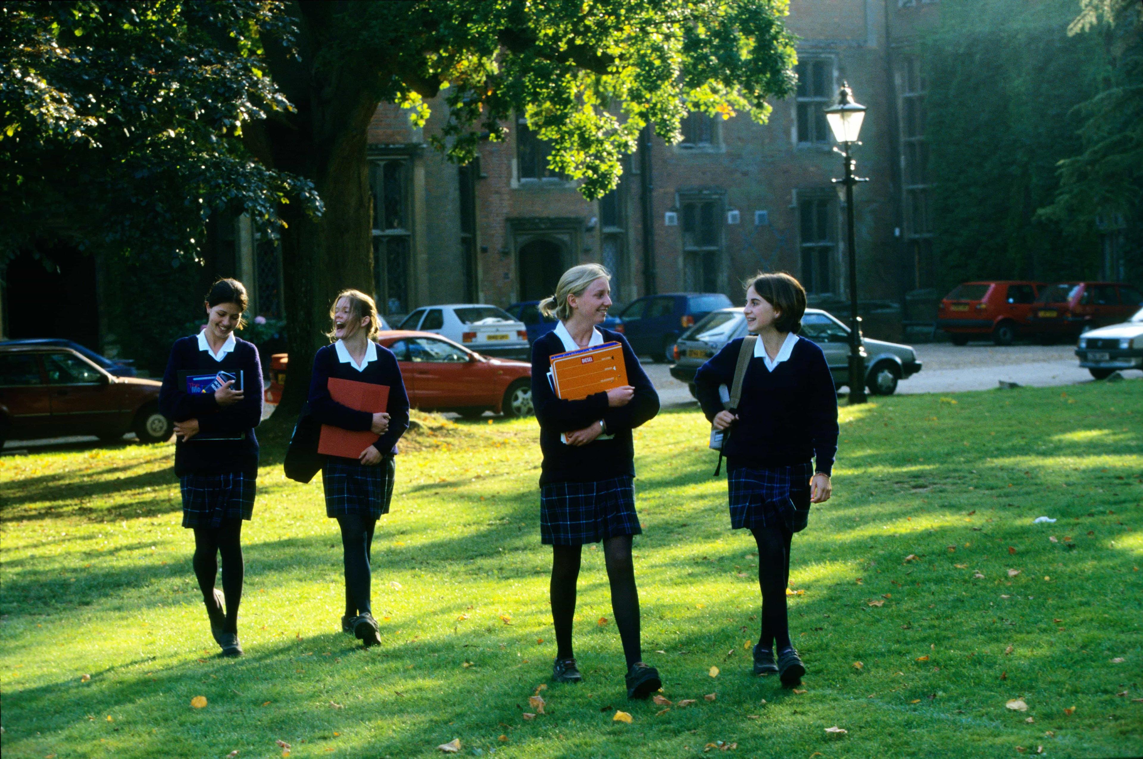 Female IGCSE students walking with notebooks and heading to their next class at school.