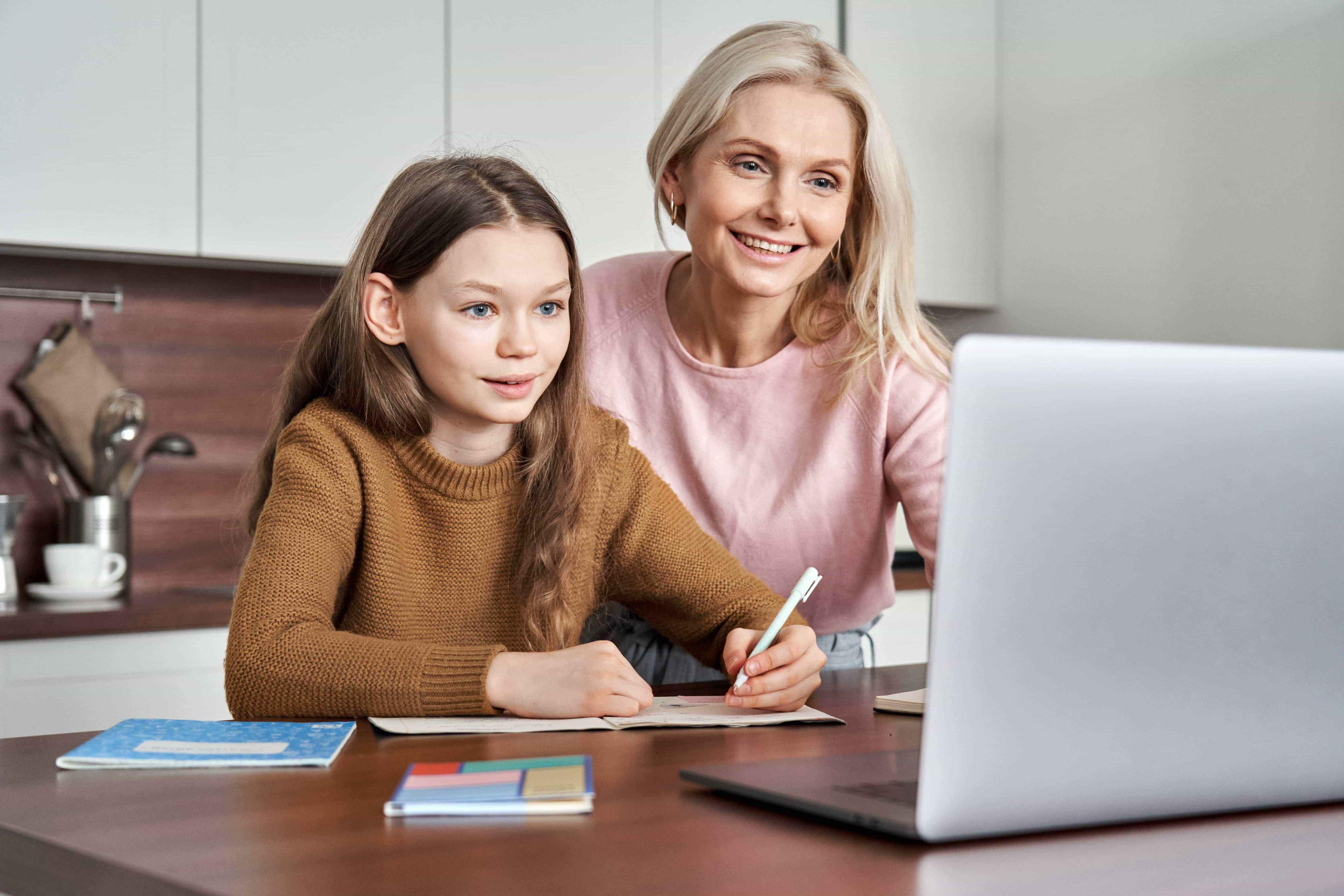 A mother and her daughter smile at their computer screen during a call with thei education advisor.