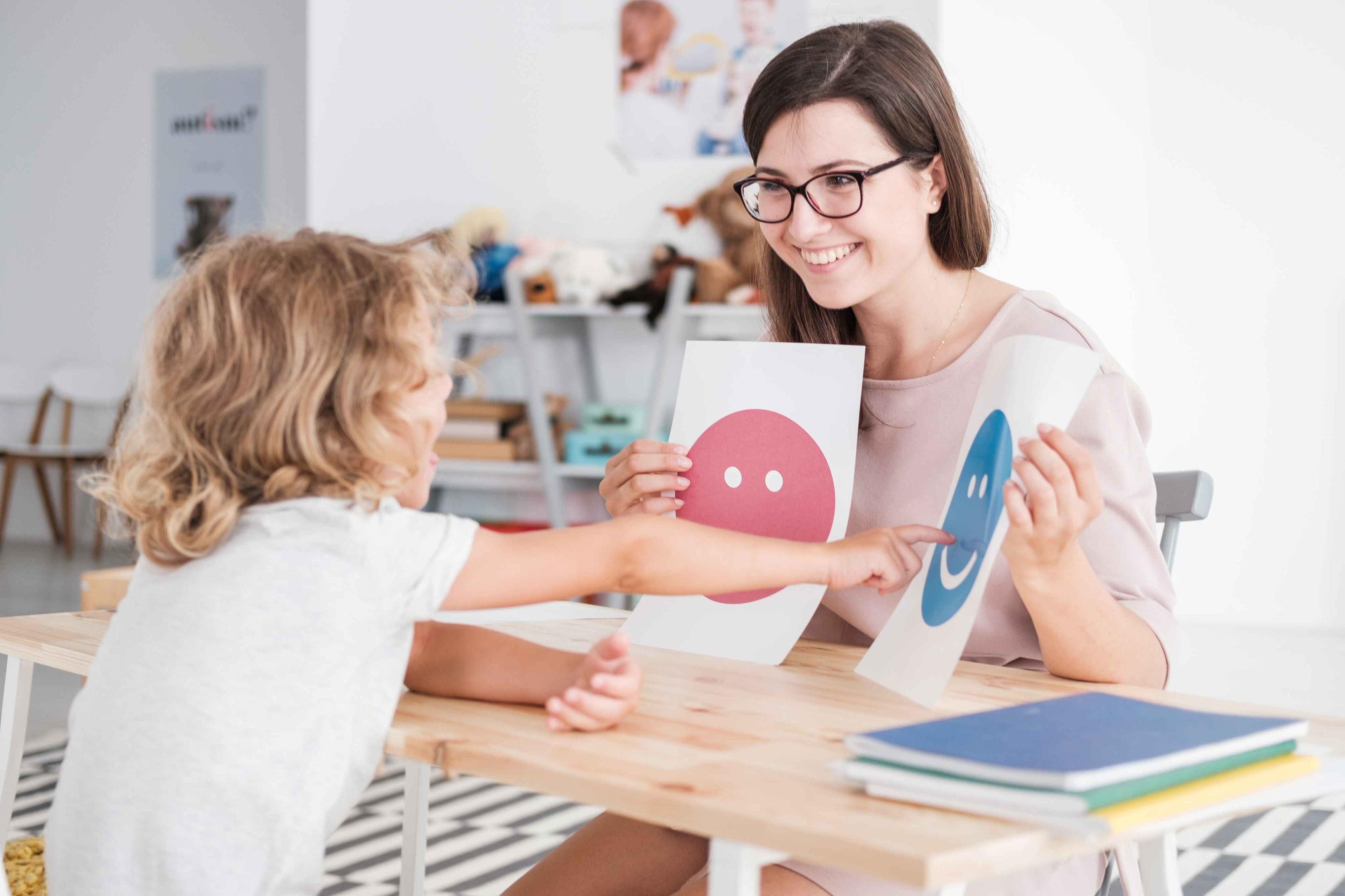 Teacher assisting a young child with emotional learning using smiley face cards