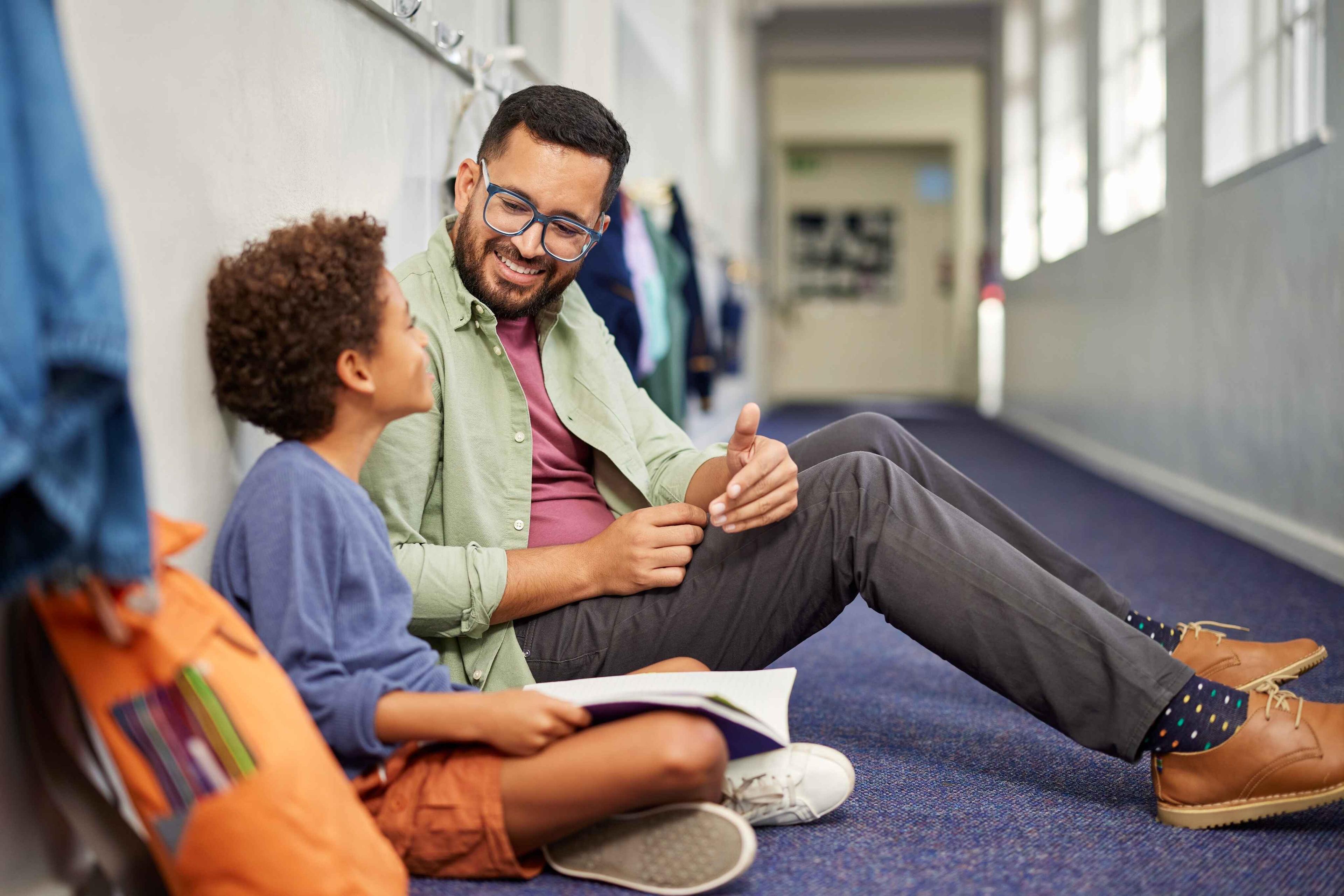 An academic coach explains something to a student seated in front of him, offering support and guidance.