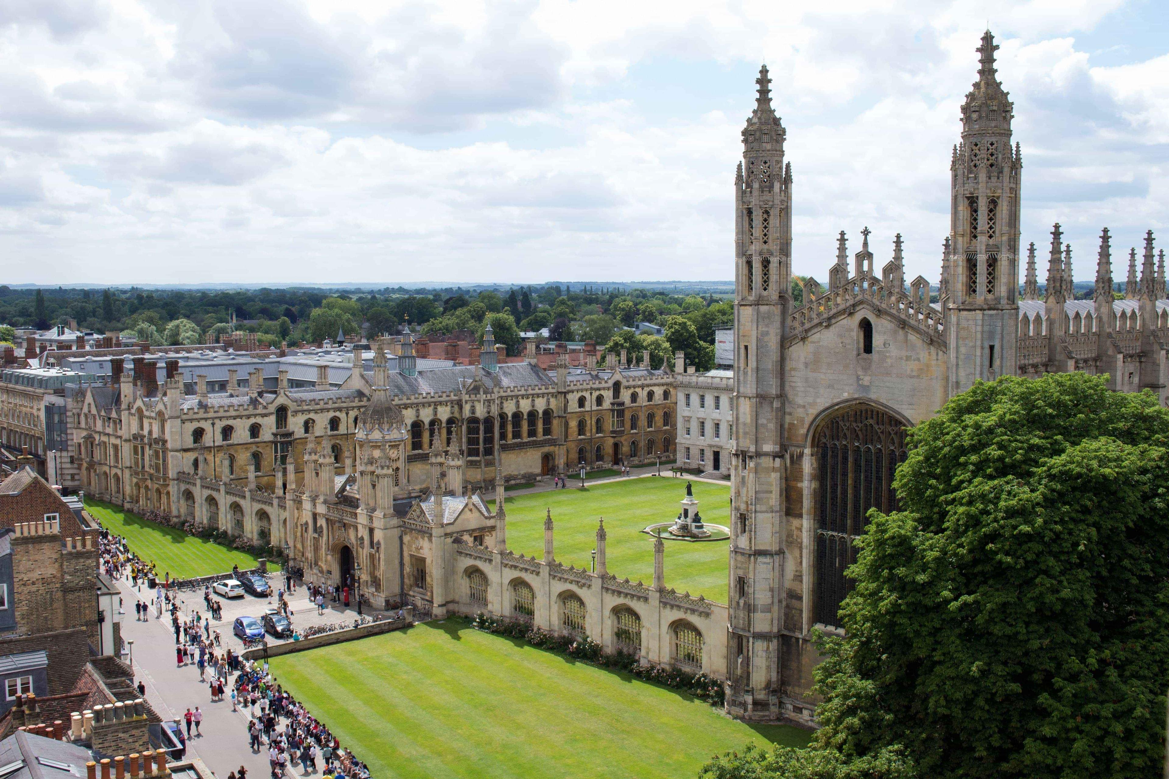 A historic Oxbridge university building with a lawned courtyard stands tall in the sunshine.