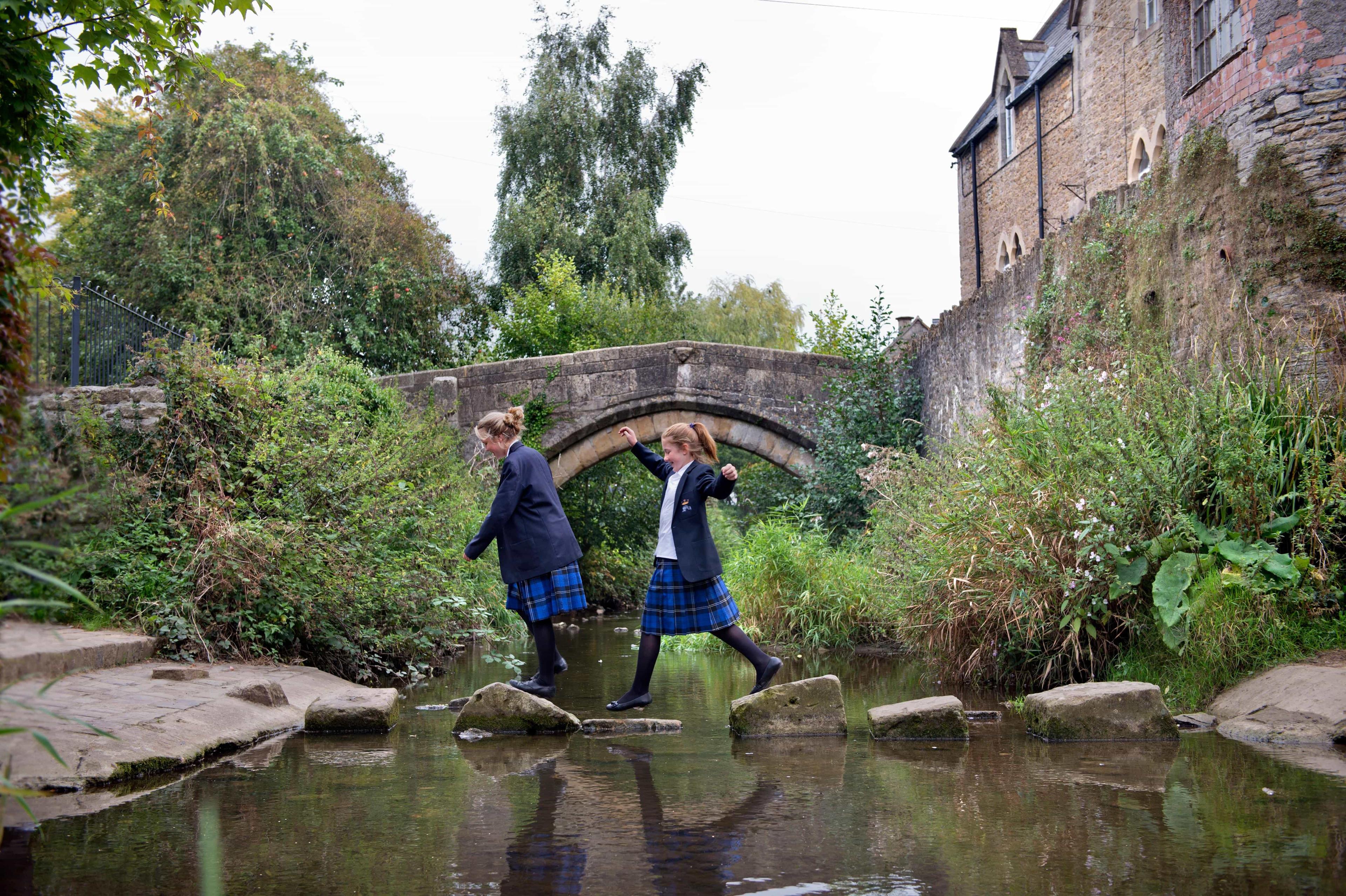 GCSE students step across stones over a stream that runs through the grounds of their British independent school.