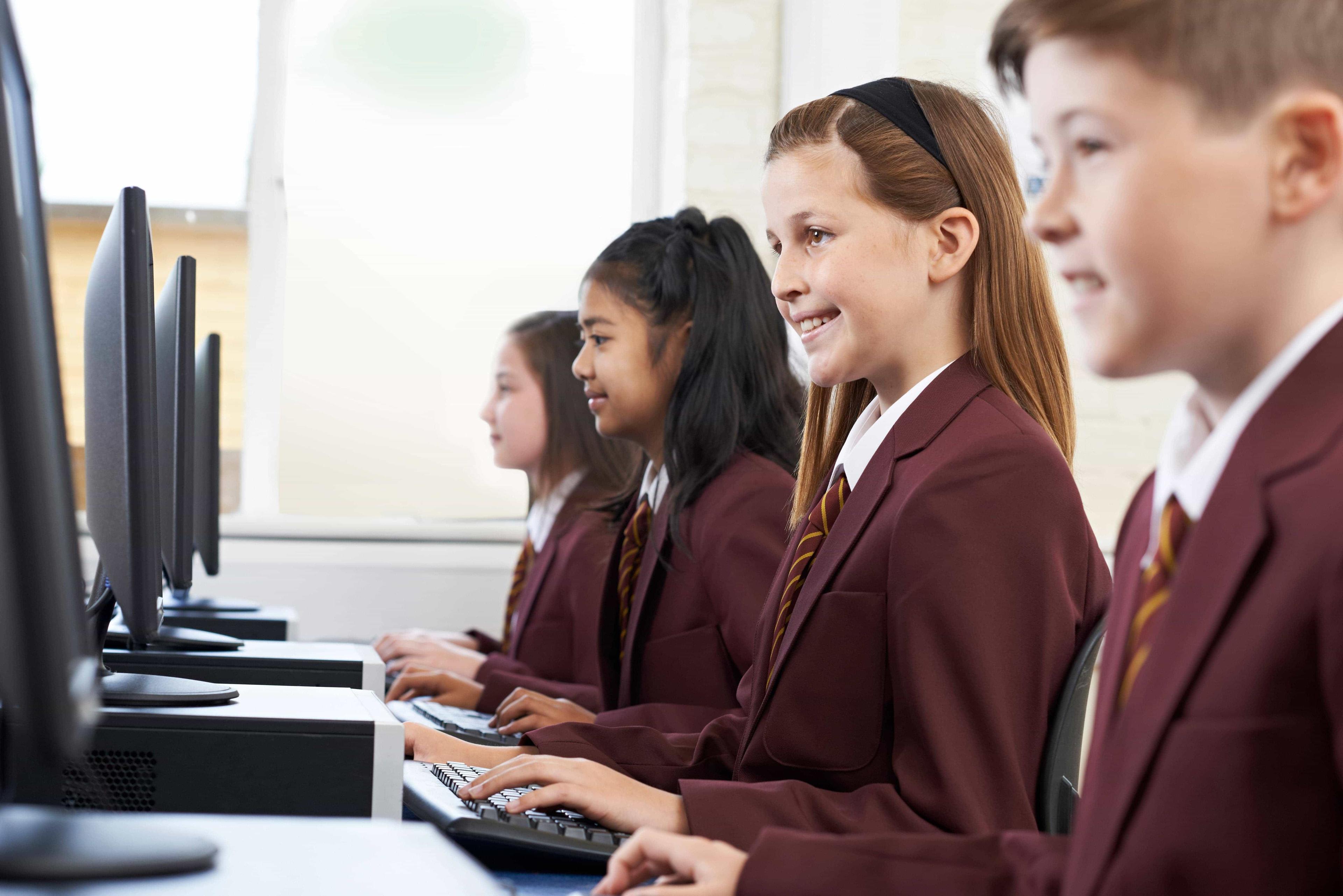 GCSE students sit attentively, listening to their online tutor while typing on their computers. 