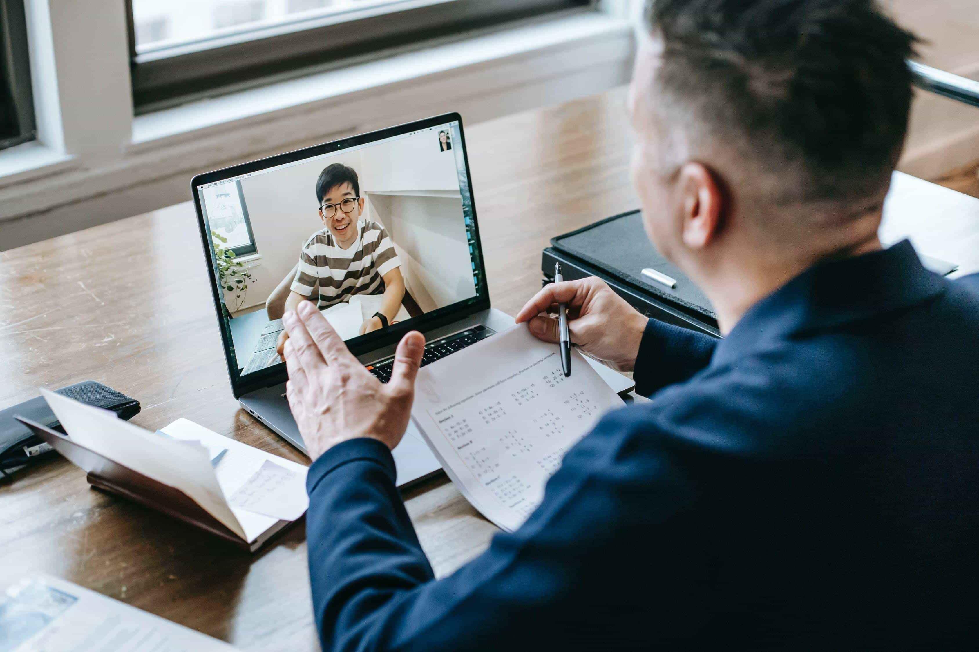 An online Maths tutor provides a private one-to-one lesson to his A level student via his laptop.