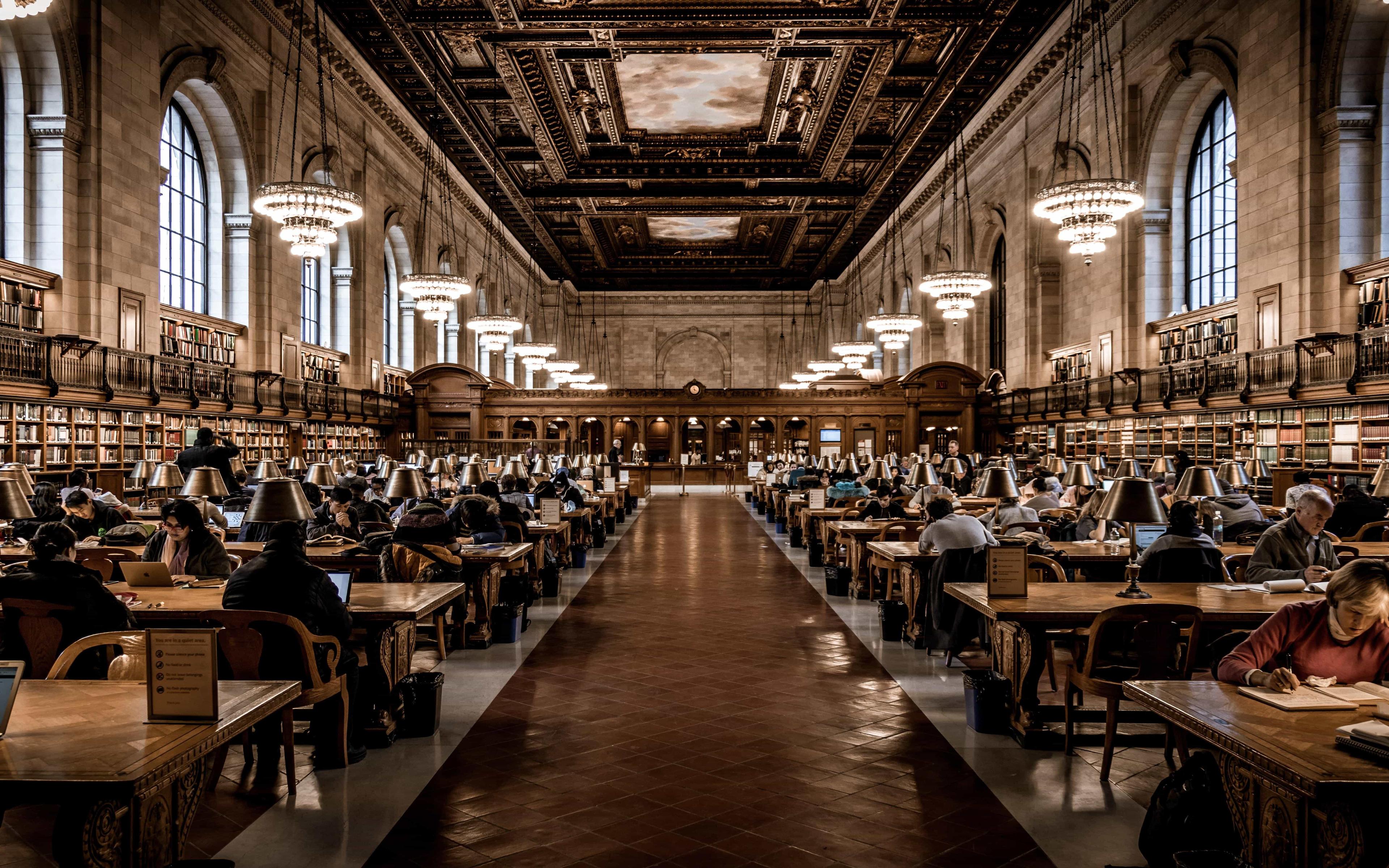 A busy UK university library filled with tables and students engaged in revision.